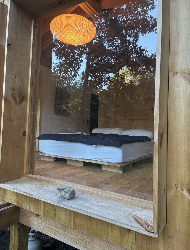 Looking through the window at the bed, with a glowing paper lantern above and trees reflected in the glass
