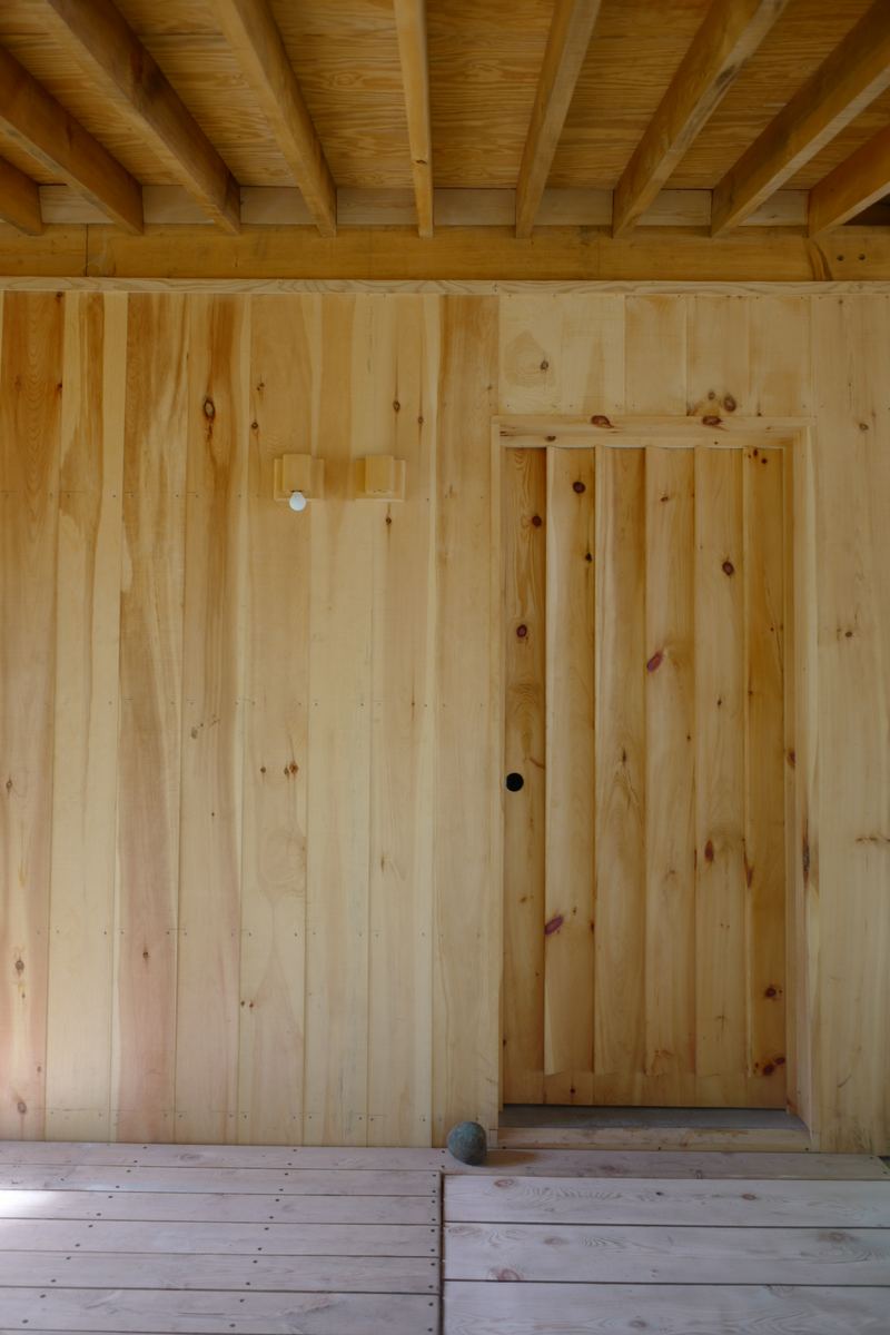 A plank door set flush into a wall of vertical pine boards, opening onto the porch deck
