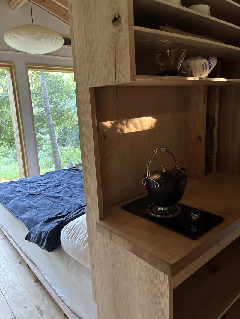 The black kettle on the stove, with the bed and tall windows beyond