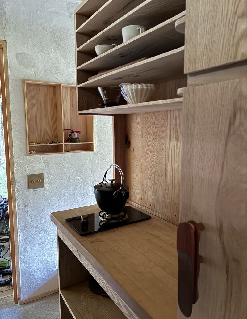 Oak kitchen cabinetry with open shelves, cups, a pour-over coffee setup and a black kettle on a single burner